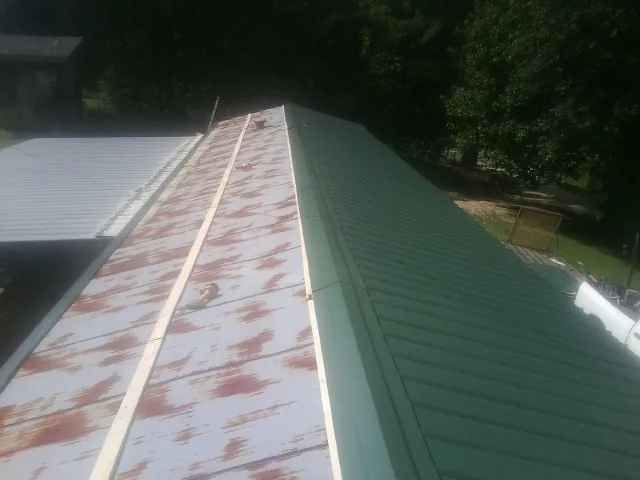 Old rusted panels beside newly installed green metal roofing — Wind Damage Roof Repair by Roofing Brothers in Superior