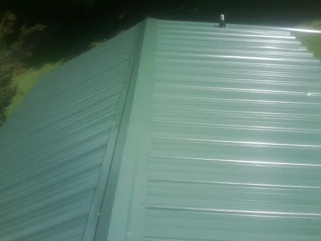 New green metal panels meeting at the ridge of a roof — Flat Roof Repair work by our crew in Superior