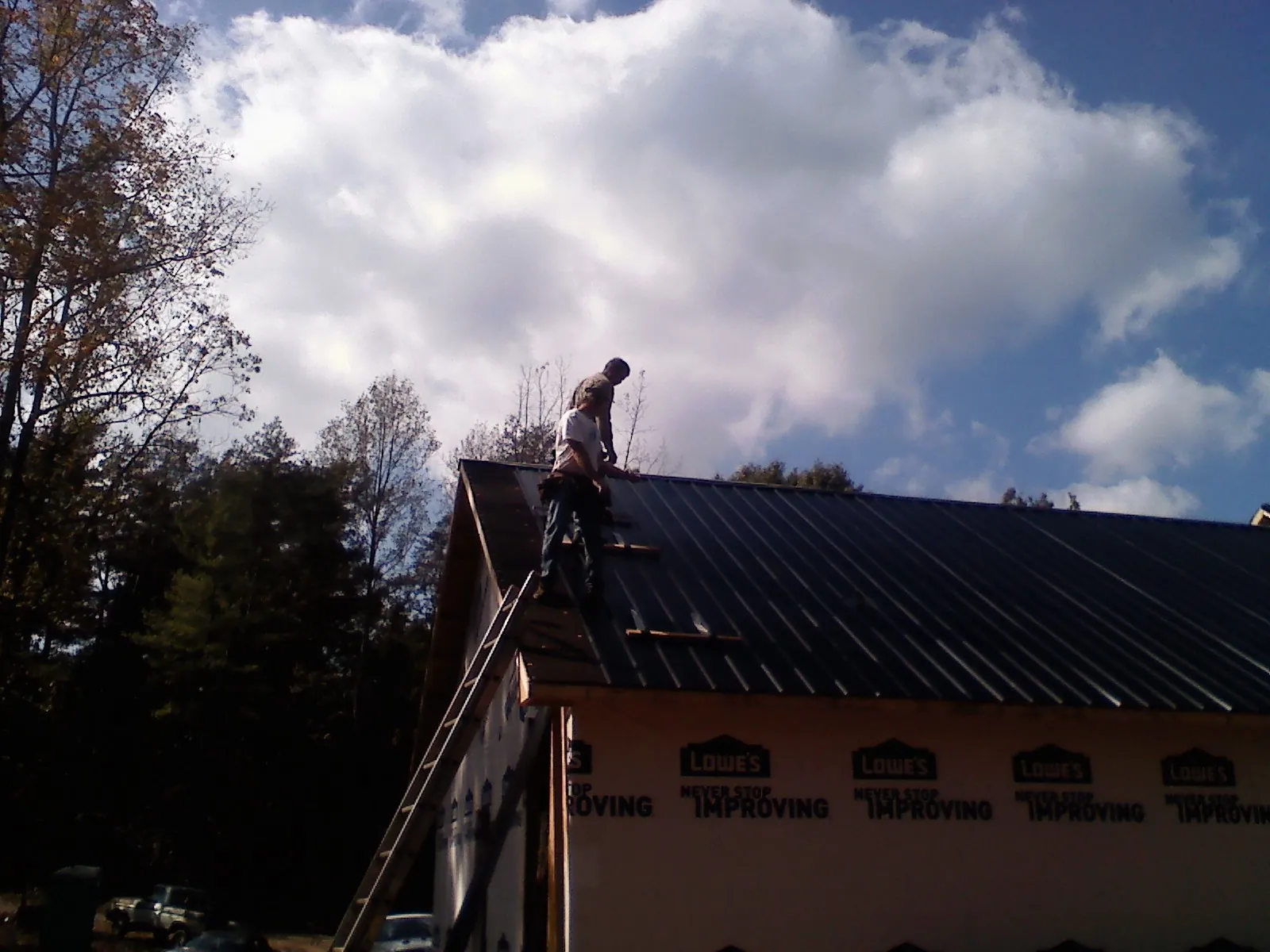 Roofer fastening dark metal panels high against a cloudy sky, from a Roof Inspection job in Superior