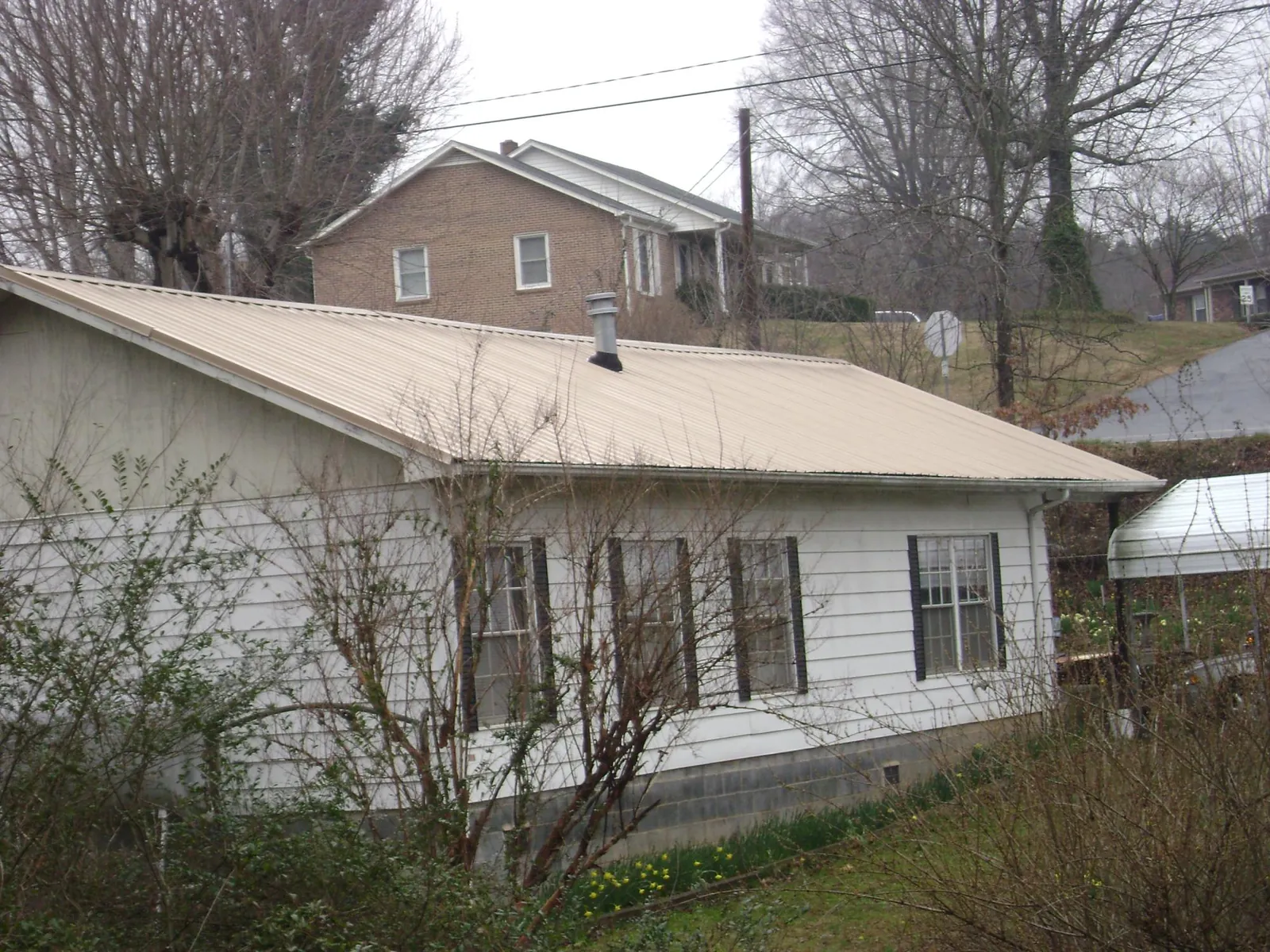 Tan metal roof on a white sided house set into a hillside — Commercial Roofing by Roofing Brothers in Superior